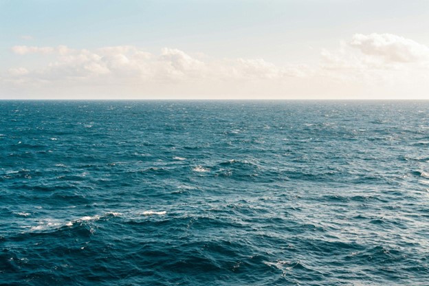 A vast expanse of ocean water under a partly cloudy sky with gentle waves on the surface