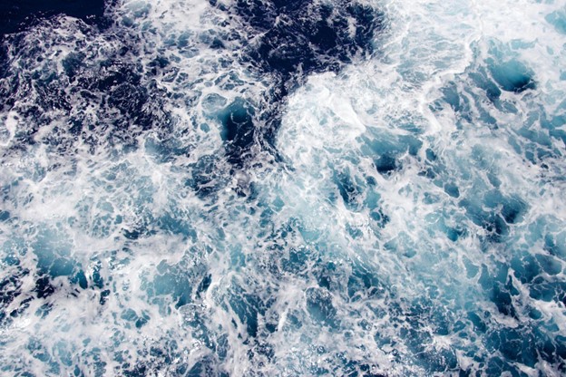 Aerial view of ocean waves creating white foam and turbulence as they crash and mix with the deep blue water